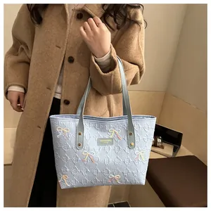 Detailed view of light blue tote bag with embossed letters and beaded bow decorations