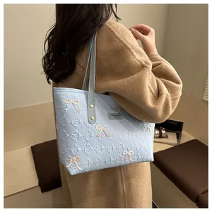 Detail of light blue tote bag featuring embossed E-pattern and colorful bow embroidery