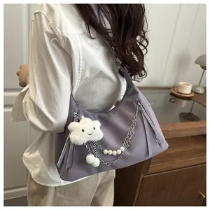 Detail der lila Nylon-Schultertasche mit süßem Wolkenanhänger und dekorativer Perlenkette