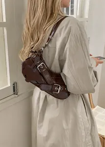 Close-up of brown leather underarm bag with decorative belts and silver buckles