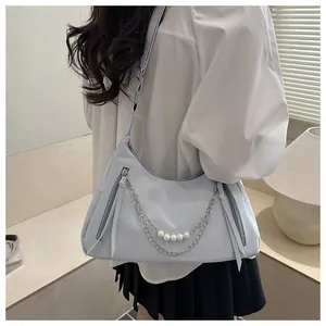 Detail der hellblauen sichelförmigen Schultertasche mit Perlenkette und langen Zippern