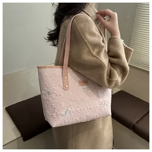 Detail of pink quilted tote bag featuring embroidered bows and brown leather handles