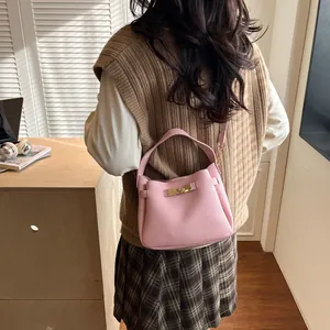 Sac seau rose en cuir à texture litchi avec fermoir doré porté dans un style de vie