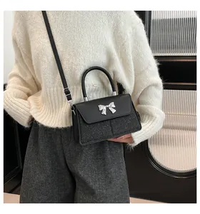 Chic black crossbody bag with silver bow accent shown on a model in a modern interior