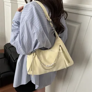 Cremefarbene Hobo-Tasche mit silbernen Ketten und Perlen, getragen von einem Modell