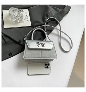 Silver sequin mini square bag with metal bow detail shown next to phone for size scale