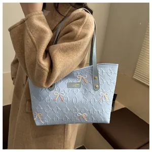Stylish light blue textured tote bag with bow details and gold hardware on female shoulder