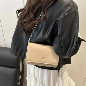 Chique beige laklederen crossbodytas met zilveren ketting gedragen door een model