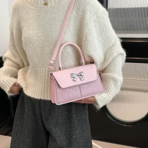 Pink bow handbag with glitter finish and crossbody strap worn by a female model
