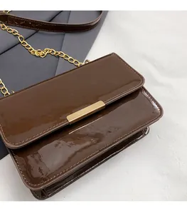 Detail of glossy brown patent leather messenger bag with elegant gold metal buckle