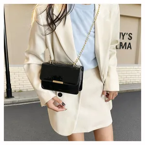 Detail of glossy black patent leather square crossbody bag with gold chain strap
