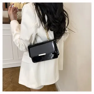 Detail of a black patent leather crossbody bag with gold chain strap on a white blazer