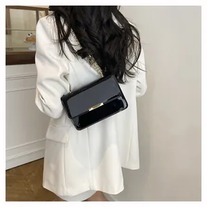 Detail of black patent leather crossbody bag featuring gold metal chain and buckle clasp
