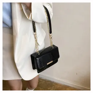 Detail of glossy black patent leather crossbody bag with elegant gold metal chain strap