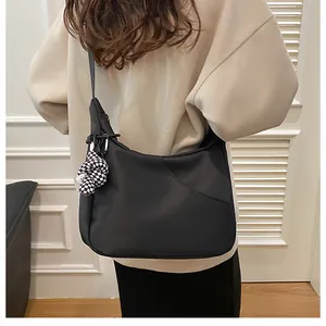 Détail d'un sac bandoulière noir en demi-lune avec un charme de nœud à damier chic