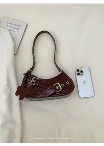 Detail view of dark brown leather underarm bag with metal buckle straps and dog pendant