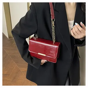 Close-up of a burgundy patent leather crossbody bag with a gold metal bar buckle and chain strap