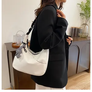 Détail du sac hobo blanc avec chaîne noire et ruban à carreaux porté à l'épaule