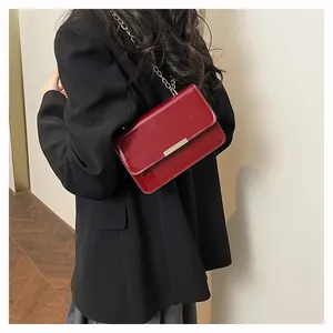 Deep red patent leather crossbody bag with gold chain strap shown on model's shoulder