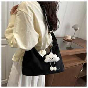 Close-up of black canvas shoulder bag with a plush cloud charm on a model's arm