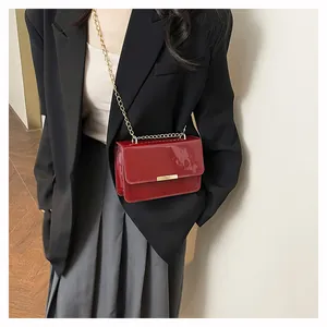 Detail of red patent leather crossbody bag with glossy finish and gold chain strap