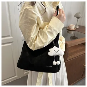 Detail of black canvas shoulder bag with white cloud plush pendant and printed logo