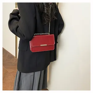 Detail of red patent leather crossbody bag with gold chain strap on a model back view
