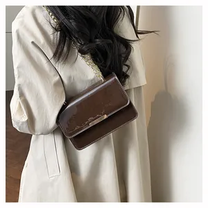 Detailed view of deep brown glossy patent leather crossbody bag with golden chain strap