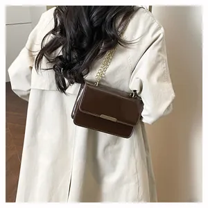 Close-up of dark brown patent leather crossbody bag with shiny gold chain and metal clasp