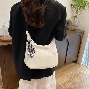 Sac hobo blanc minimaliste en cuir avec breloque à carreaux porté par un mannequin