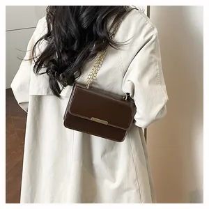 Detail shot of a dark brown patent leather crossbody bag with elegant gold chain and bar strap