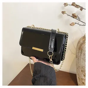 Detail shot of black patent leather crossbody bag with gold hardware and chain strap