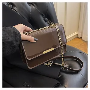 Detail of dark brown patent leather crossbody bag with gold metal trim and chain strap