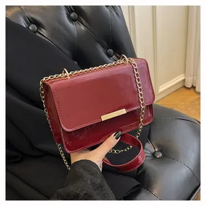 Detail of burgundy patent leather crossbody bag with gold chain and metal bar accent