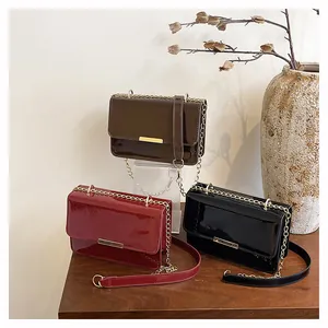 Three patent leather crossbody bags in red, black, and brown with gold chain straps
