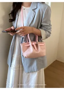 Detail view of a pink woven leather bucket bag with a decorative buckle and thin strap