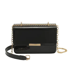 Fashionable black patent leather crossbody square bag with gold chain strap on white background