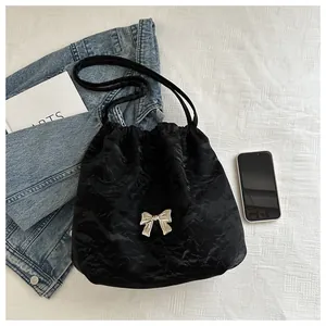 Detail of black pleated bucket bag with a metallic silver bow on satin fabric