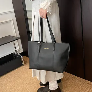 Classic black faux leather tote bag with gold lettering shown in a stylish hand-carry pose