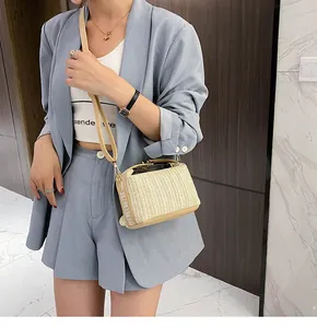 Detail of a beige woven straw crossbody bag with light brown leather trim and gold buckle