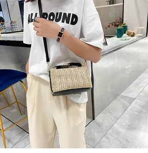 Close-up of a woven straw crossbody bag with black leather base and metallic buckle