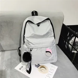 Detail of light gray nylon backpack with brand logo and soft black plush pompom charm