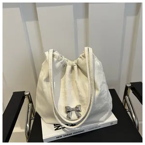 Detail view of cream bucket bag featuring a silver bow and pleated leather texture
