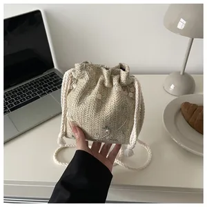 Detail der beigen geflochtenen Beuteltasche mit rosa Blumenstickerei und Kordelzugband