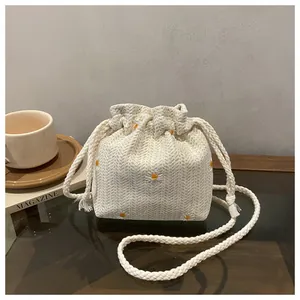 Dettaglio della borsa a secchiello color crema con ricamo di margherite e tracolla in corda