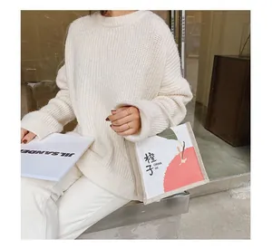 Close-up of white canvas tote bag with orange print and a chunky knit sweater