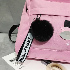 Close-up of pink nylon backpack featuring leaf embroidery and black plush pompom charm