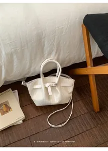 Lifestyle shot of a cream-white woven bucket bag with elegant metal buckle on wood floor