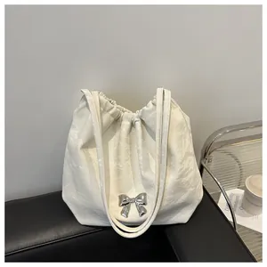 Detail of off-white leather bucket bag with silver bow on a black leather sofa