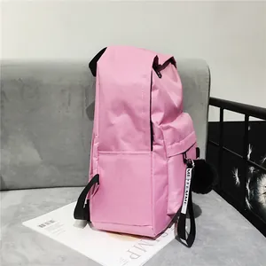 Detail view of pink nylon backpack featuring a soft black pompom charm and side water bottle pocket